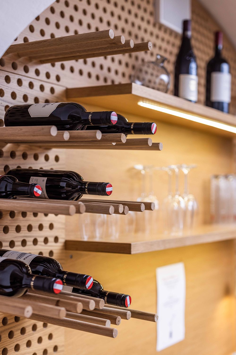 A wooden wine rack on the wall of the hotel bar with bottles of red wine