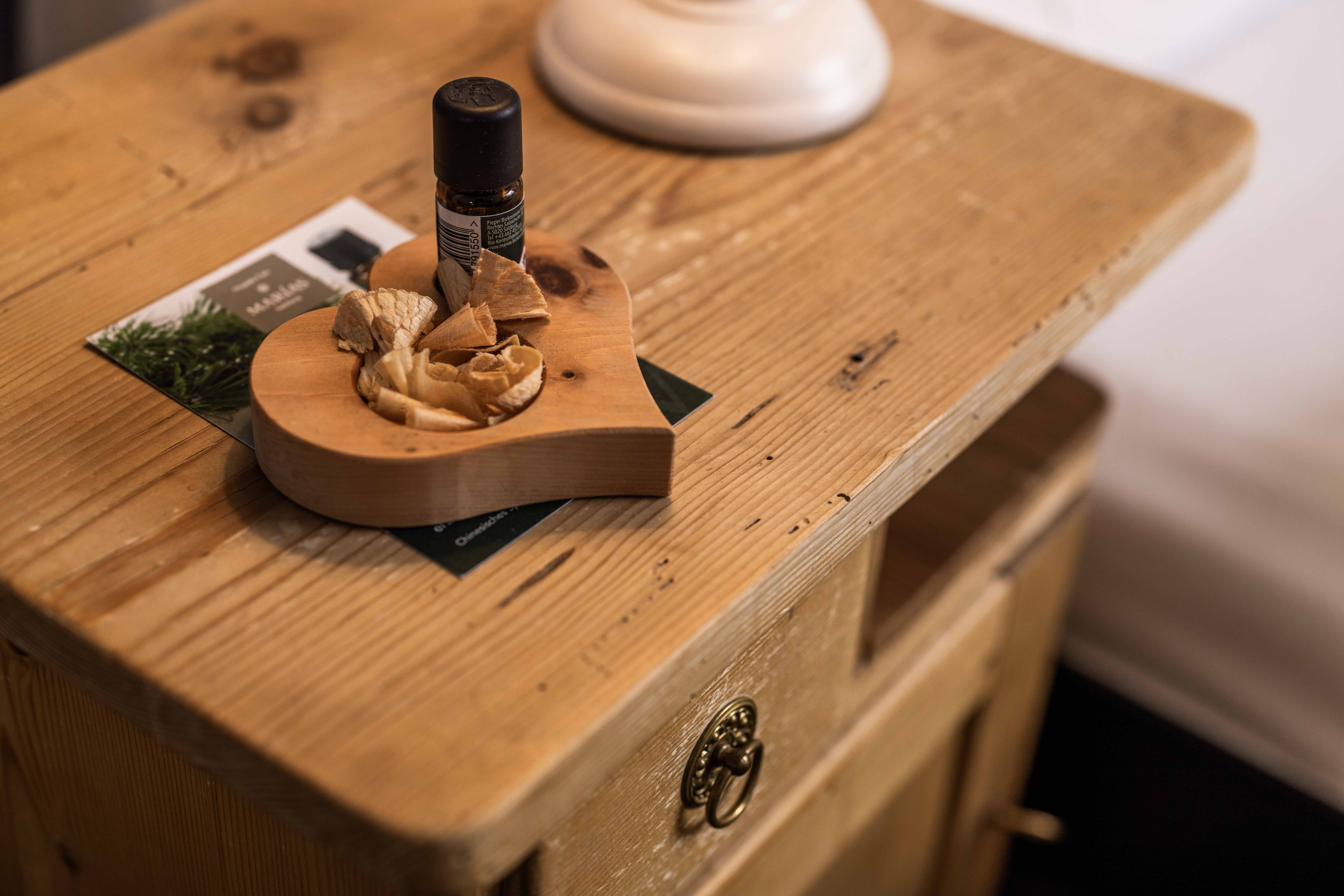 A vial of essential oil next to a scented bowl on a rustic dresser