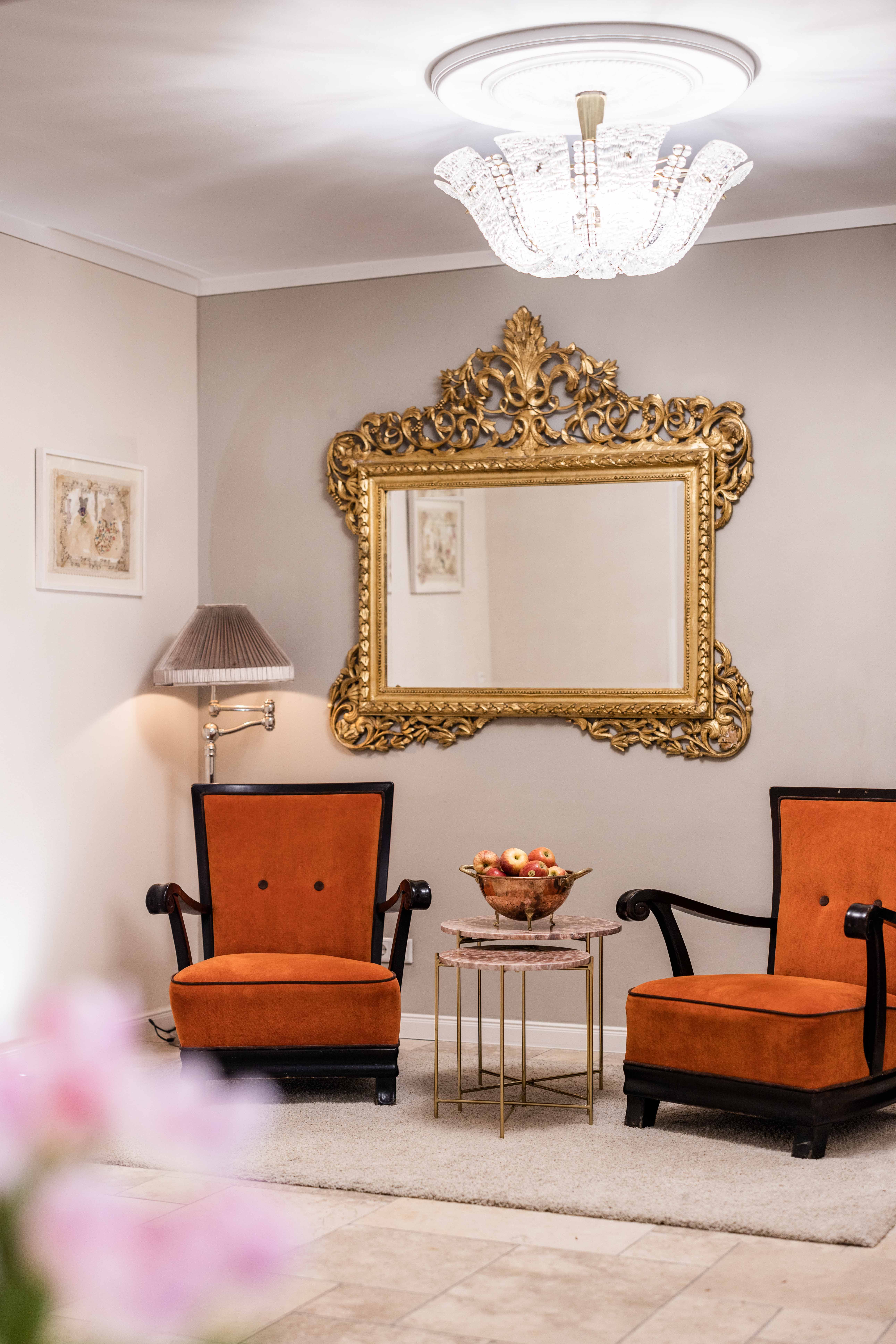 Elegant hotel lobby with orange upholstered armchairs and a gold mirror on the wall